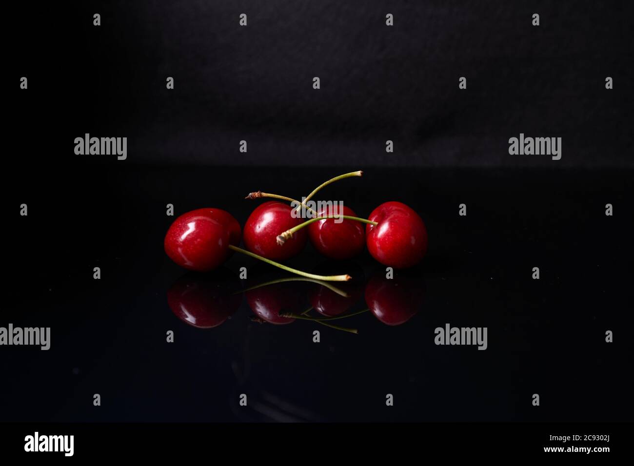 reflection of four cherries on black background Stock Photo