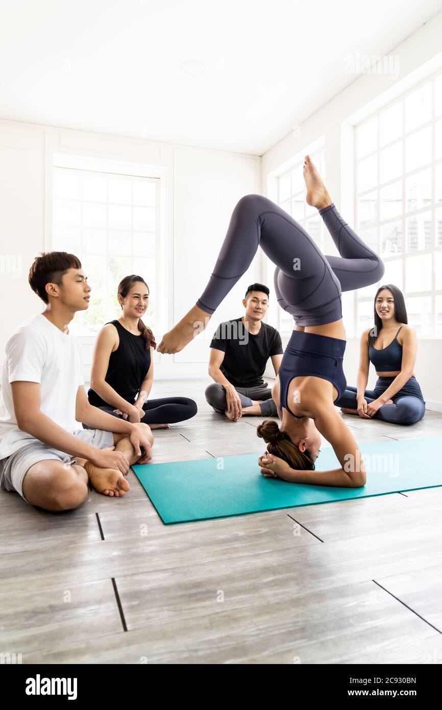 Asian yoga female coach or instructor wear sportswear bra pants show student in fitness studio class  poseture of headstand pose. Yoga Practice Work o Stock Photo
