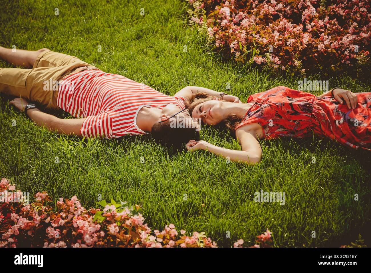 Happy young couple lying head to head on a grass with flowers. Summertime Stock Photo