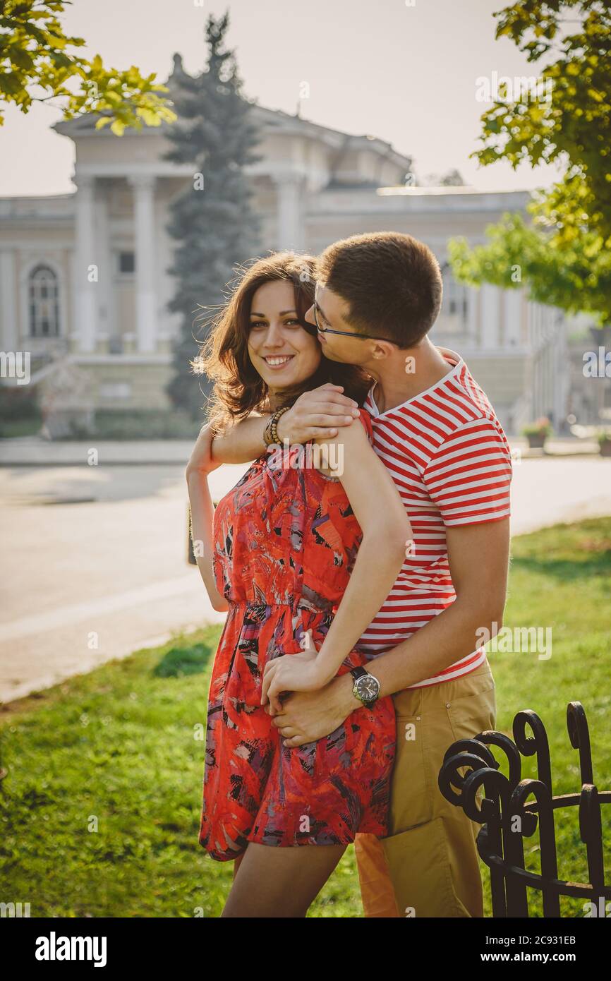 Beautiful young smiling couple in love, hugging, kissing and spending time together outdoors at green city street Stock Photo