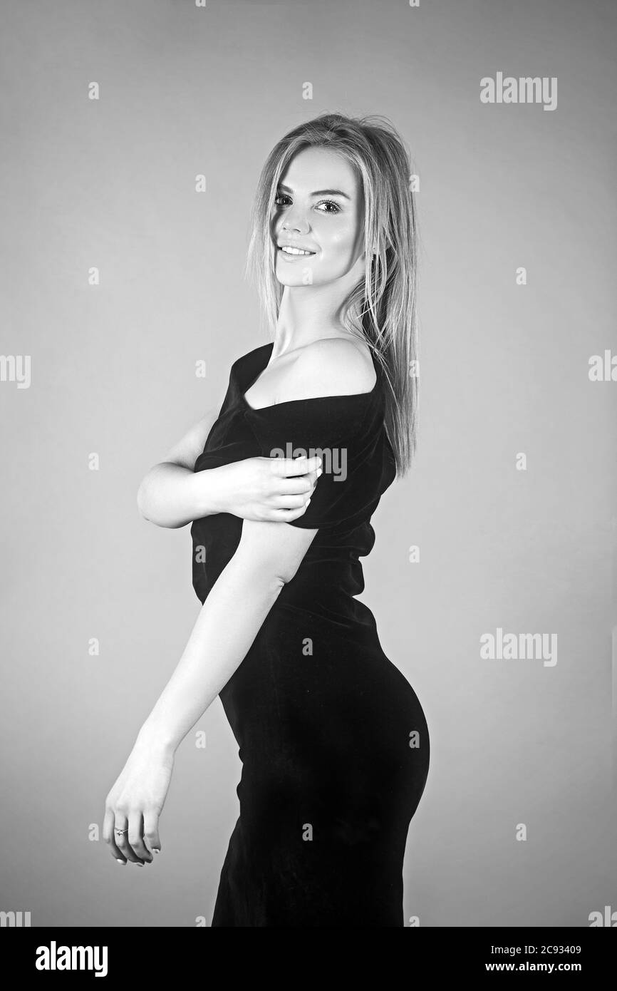 Young blonde lady in black dress posing on grey background. Stock Photo