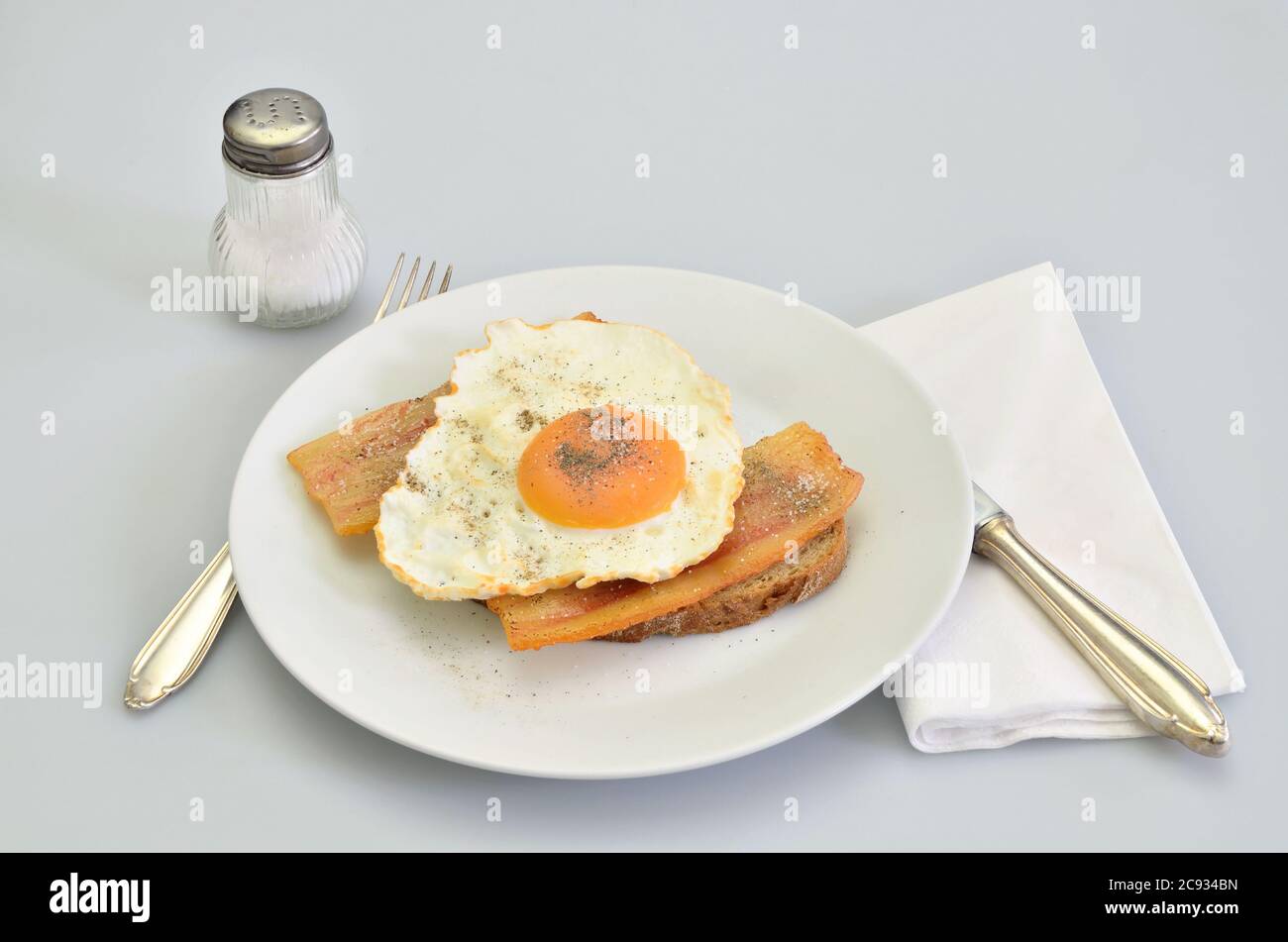 sandwich with bacon and fried egg with salt and pepper on white plate, closeup, isolated on white background Stock Photo