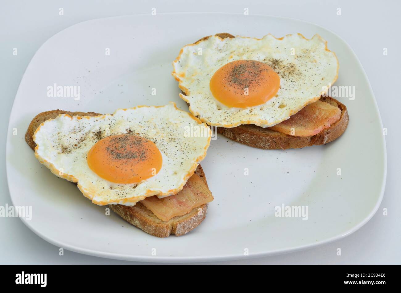 two sandwiches with bacon and fried egg with salt and pepper on white plate, closeup, isolated on white background Stock Photo