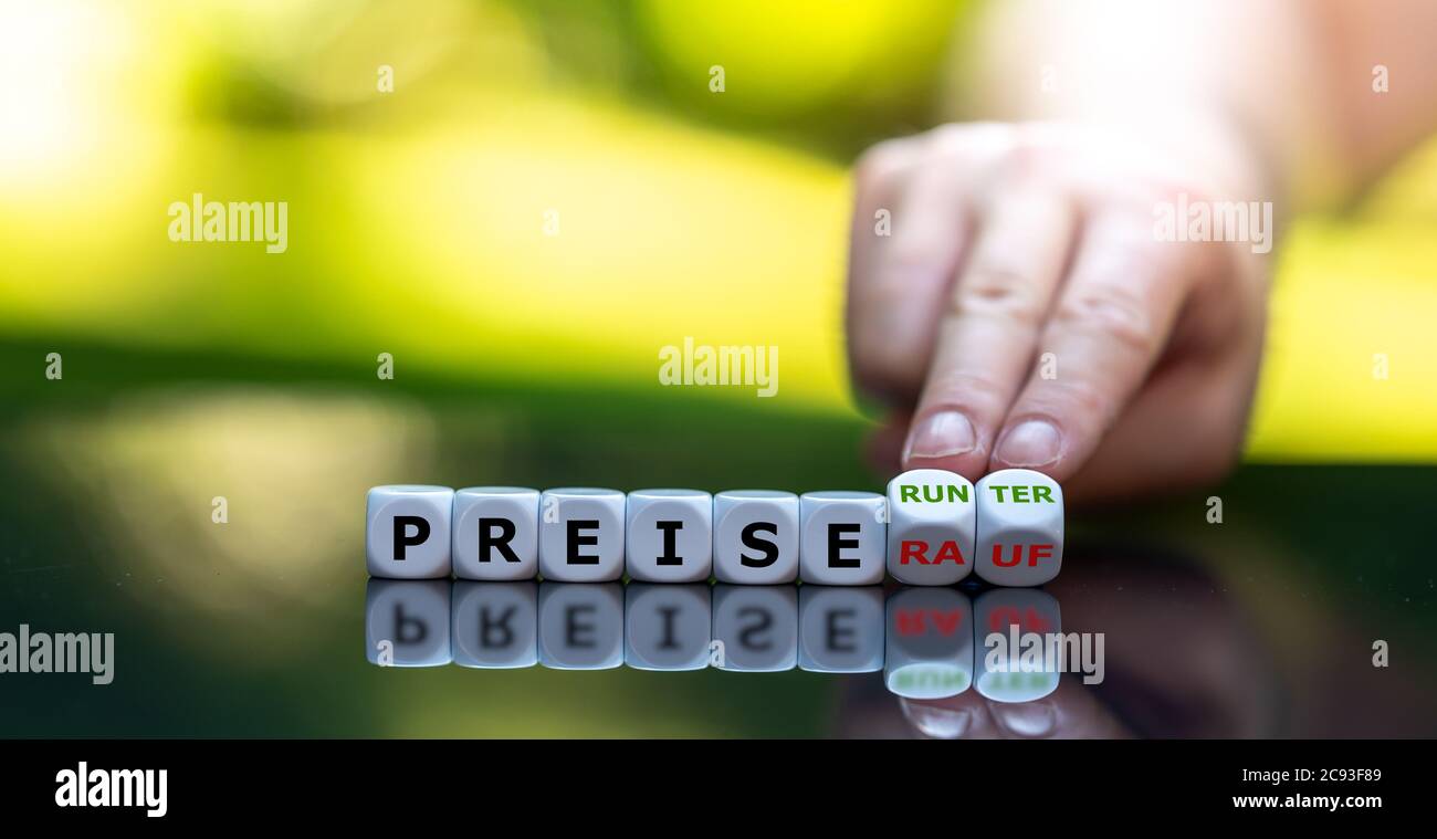 Hand turns dice and changes the German expression 'Preise rauf' (price up) to 'Preise runter' (price down). Stock Photo