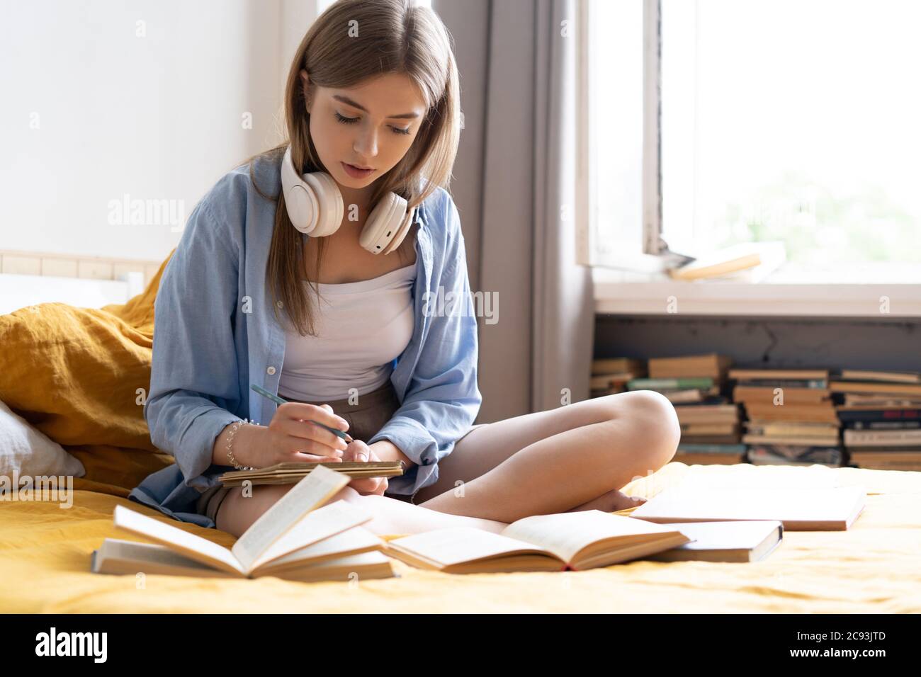 Attractive student woman laying on her bed at home while writing and working on her homework from college Stock Photo