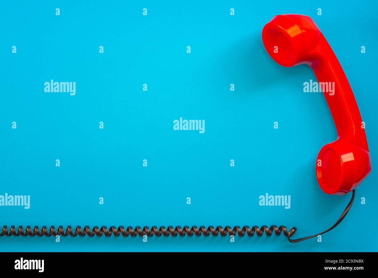 Contact us concept with a vintage red telephone handset next to the curly phone cable isolated on blue background with copy space Stock Photo