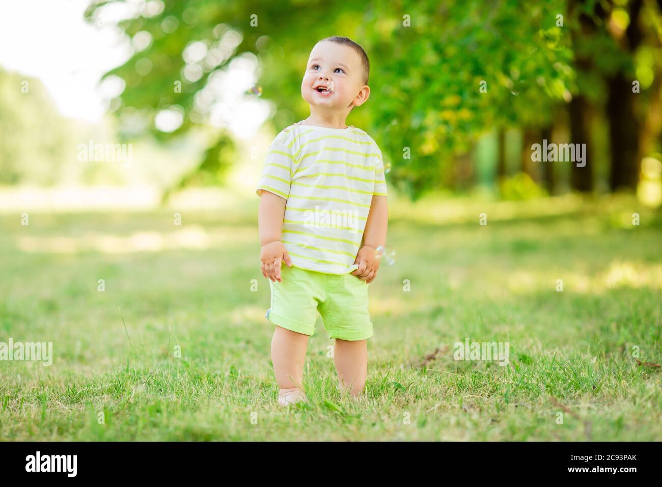 Happy baby boy one year plays with soap bubbles summer outdoors. Children's Lystyle Stock Photo