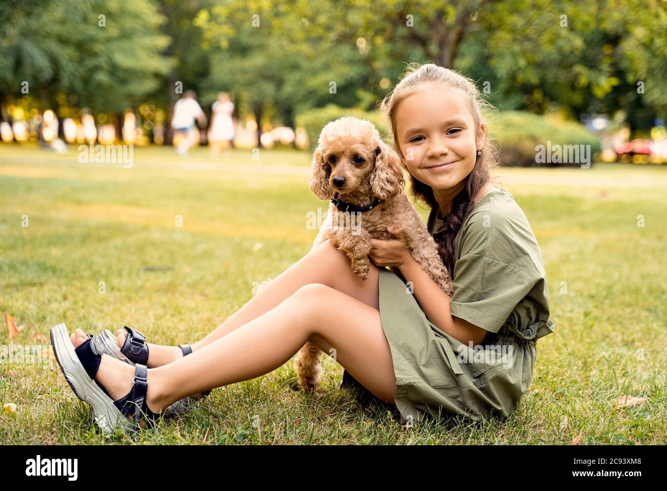a girl is sitting on a green lawn with a poodle dog Stock Photo - Alamy