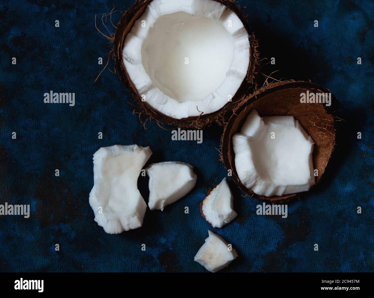 Open coconut lies on a dark blue background next to broken pieces lying randomly Stock Photo