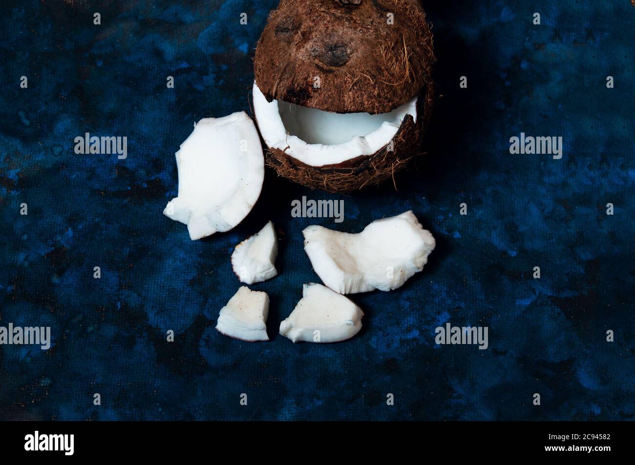 Open coconut lies on a dark blue background next to broken pieces lying randomly Stock Photo