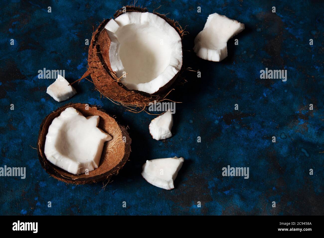 Open coconut lies on a dark blue background next to broken pieces lying randomly Stock Photo