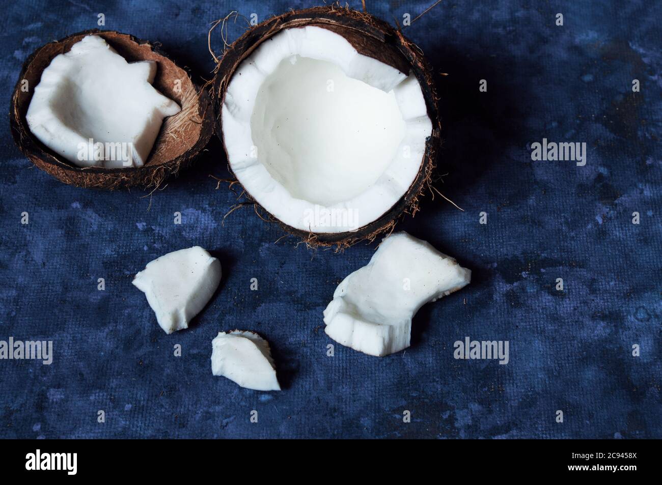 Open coconut lies on a dark blue background next to broken pieces lying randomly Stock Photo