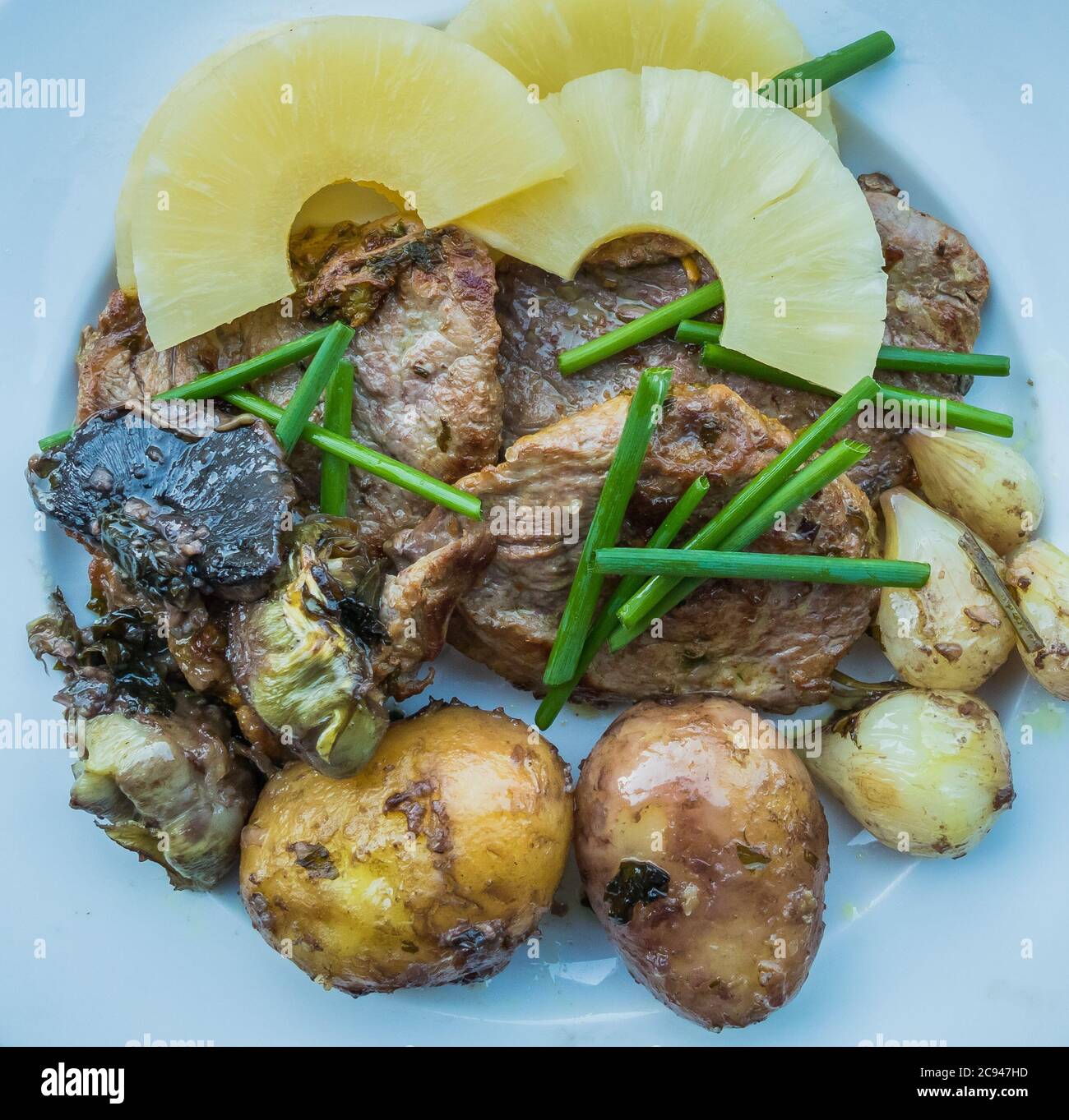 food meat with potatoes, onions, artichoke and chives and pineapple on withe plate top view Stock Photo