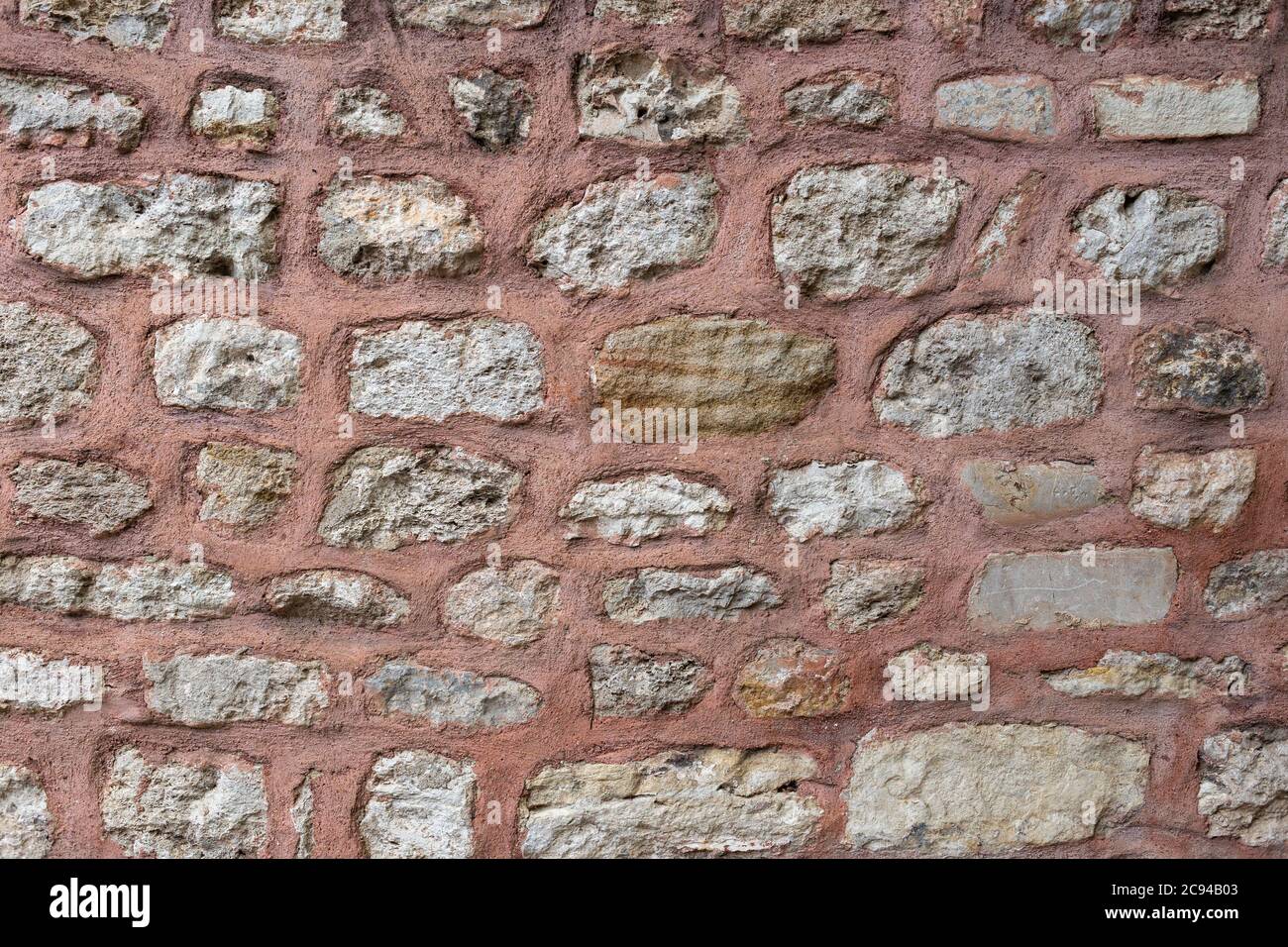 Gray stone wall texture with lime bricks pasted with red colored cement. Stock Photo