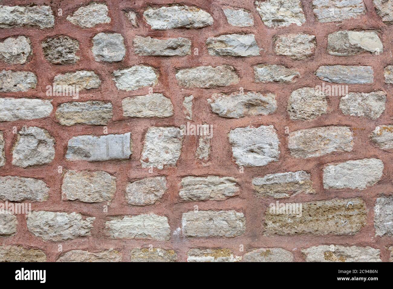 Gray stone wall texture with lime bricks pasted with red colored cement. Stock Photo
