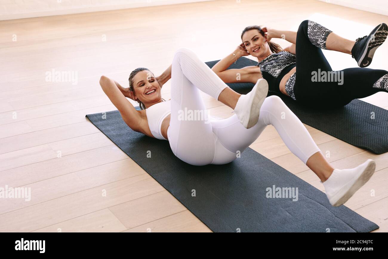 Two cheerful women lying down on fitness mat and doing abs workout