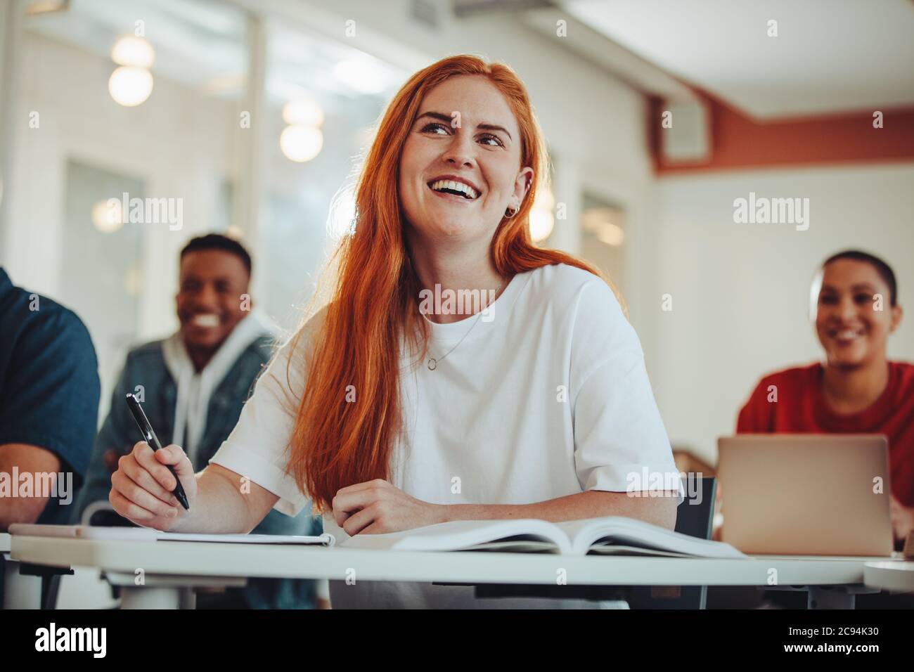 Woman paying attention in lecture. Female student listening to the teacher and smiling sitting in classroom. Stock Photo