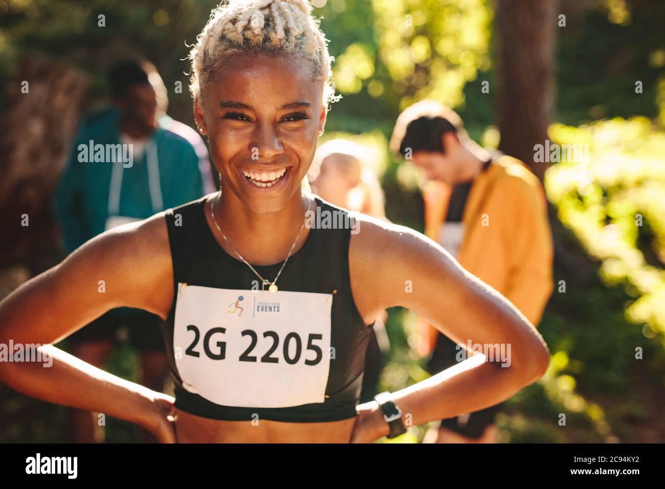 Female cross country marathon runner smiling outdoors. Sportswoman laughing outdoors with her club members in background. Stock Photo