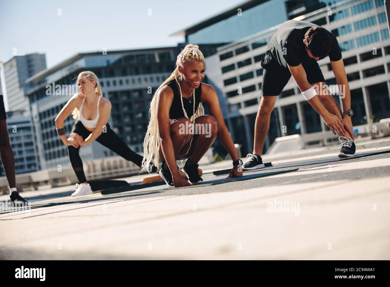 Group of people during workout session outdoors. Friends stretching on exercise mat outdoors in the city. Stock Photo
