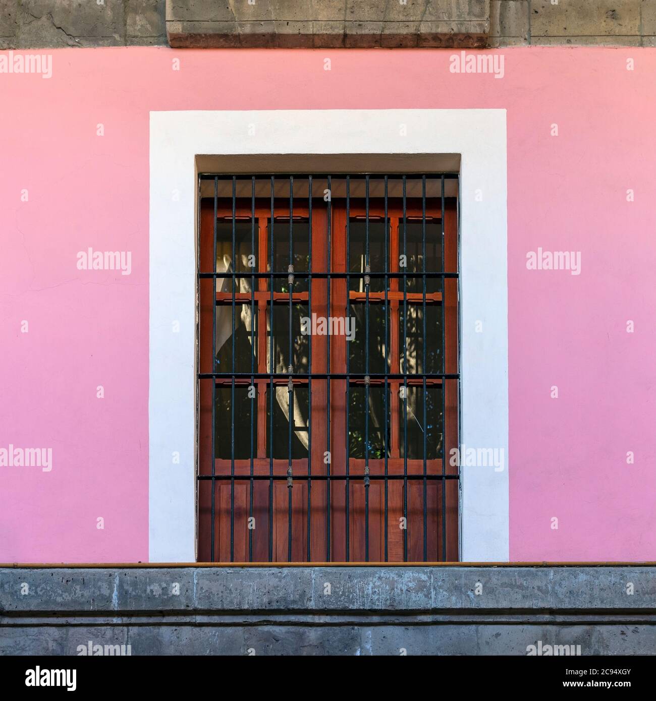 Traditional colonial style architecture in the district of Coyoacan with a wooden window frame and pink facade wall, Mexico City, Mexico. Stock Photo