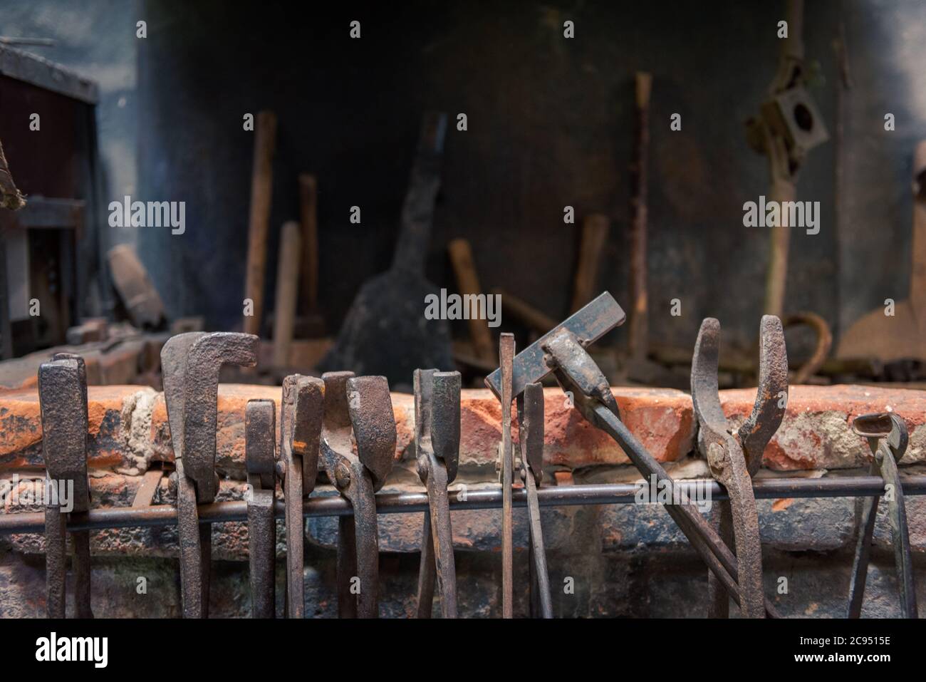 Old historic tongs and grippers of blacksmith hanging on rusty forge in front of fireplace Stock Photo