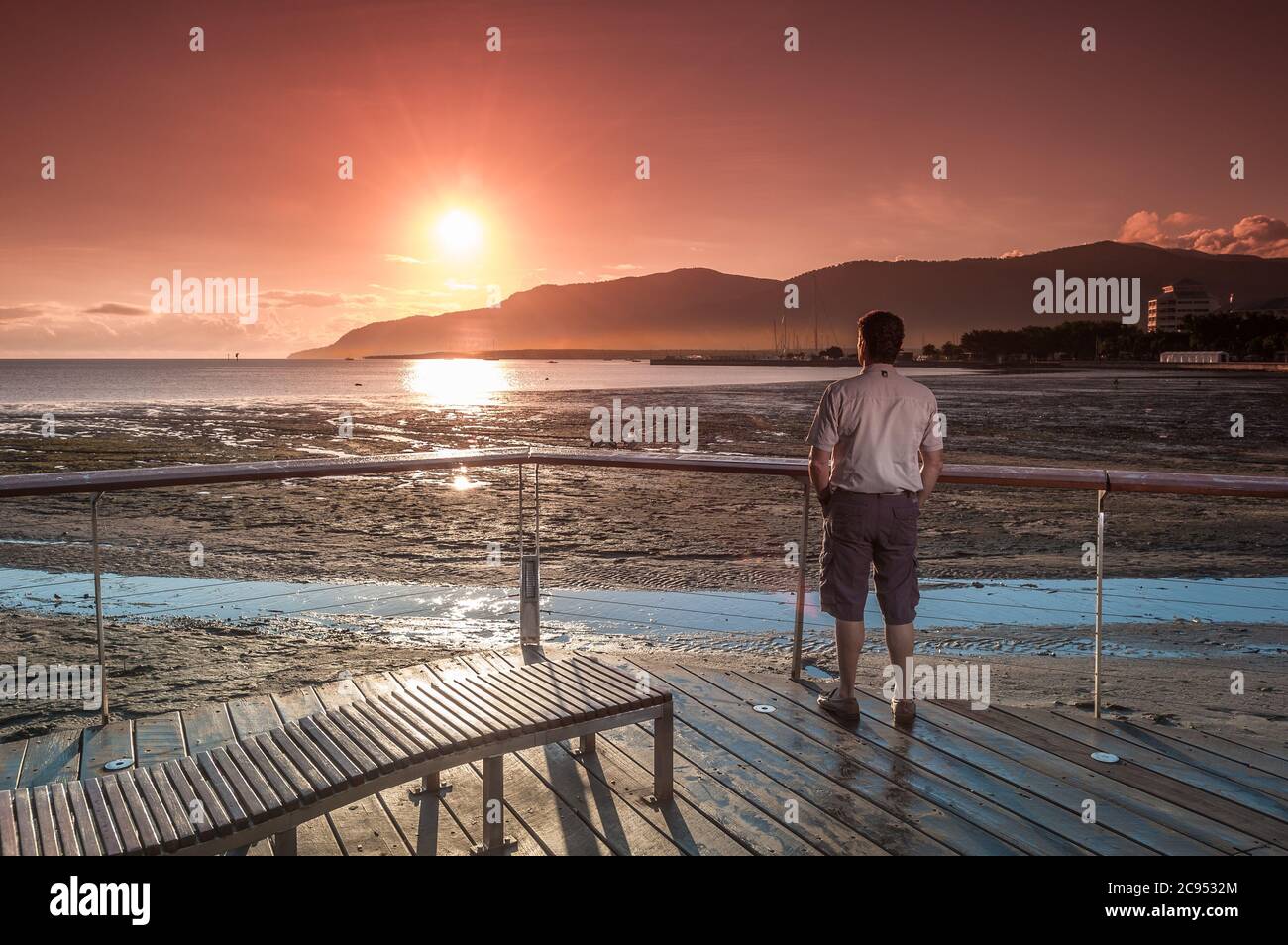 A male tourists enjoys a gorgeous scenic sunrise on the esplanade boardwalk, observation deck in Cairns, Queensland, Australia. Stock Photo