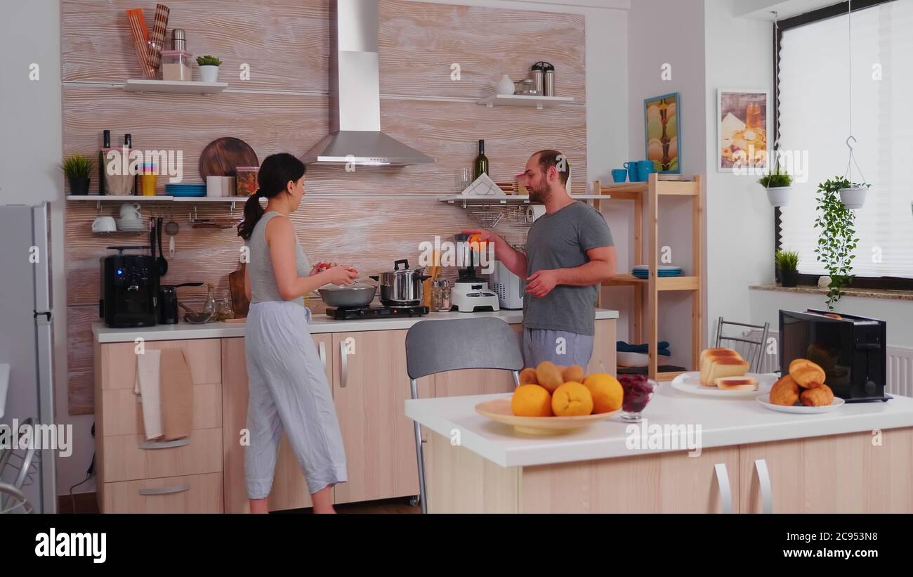 Cheerful married couple preparing breakfast and chatting. Husband having a conversation with wife while she is preparing eggs for breakfast. Stock Photo