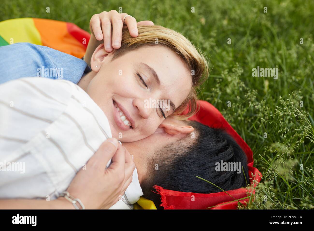 Close-up of two happy women lying on green grass and embracing they love each other Stock Photo
