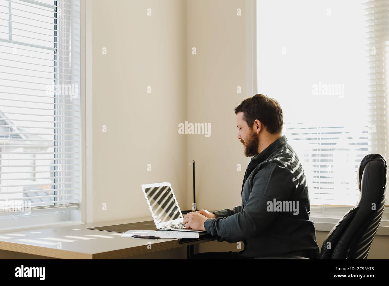 Male web developer sitting at desk and using laptop at cabinet. Stock Photo