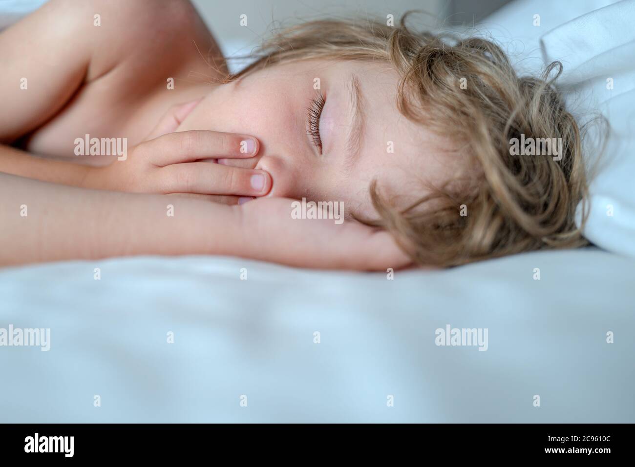 Little kids sleeping with her mouth open, snoring. Kid in bedroom sleep on bed with white sheet and pillow. Stock Photo