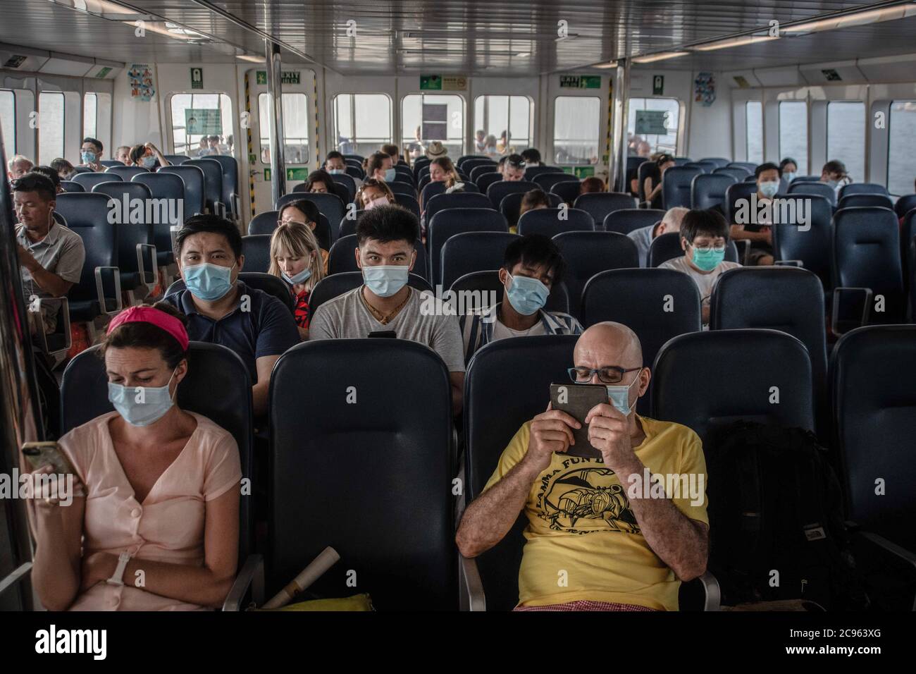 Passengers on a ferry wear surgical masks during a trip between Lamma Island and the Central district of Hong Kong. Summer 2020 is marked by the scenes related to the coronavirus pandemic. Surgical masks and warnings banning people from accessing the scenario. Stock Photo