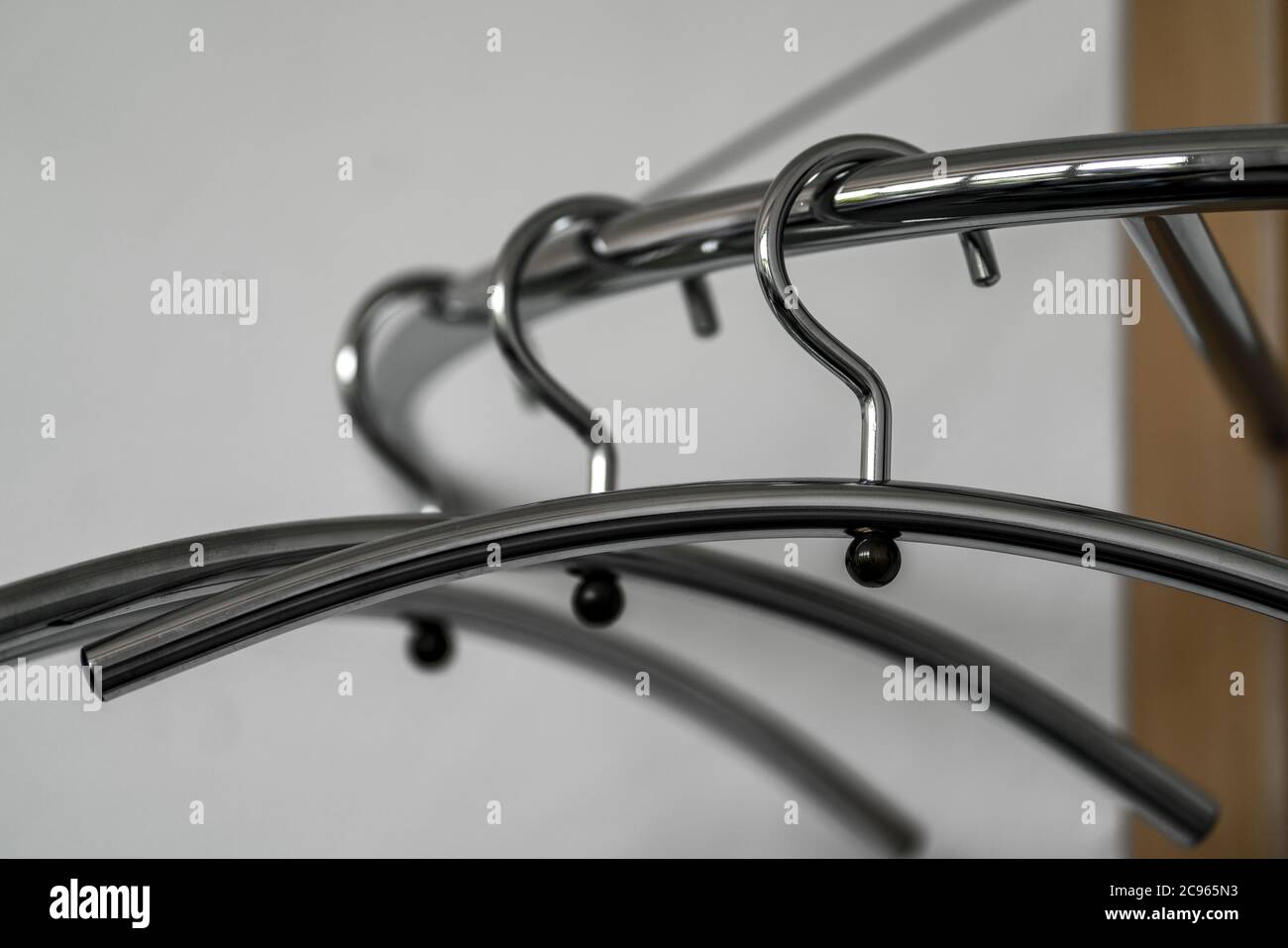 Three chrome plated hangers hanging empty from a wooden coat rack Stock Photo