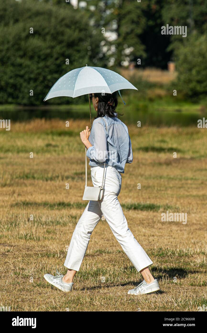 WIMBLEDON LONDON 29 July, 2020. A woman shelters under an umbrella on a