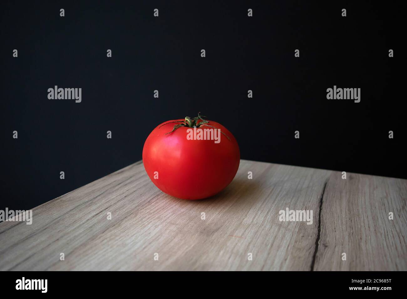 Single ripe red tomato lying on a wooden board against black background Stock Photo
