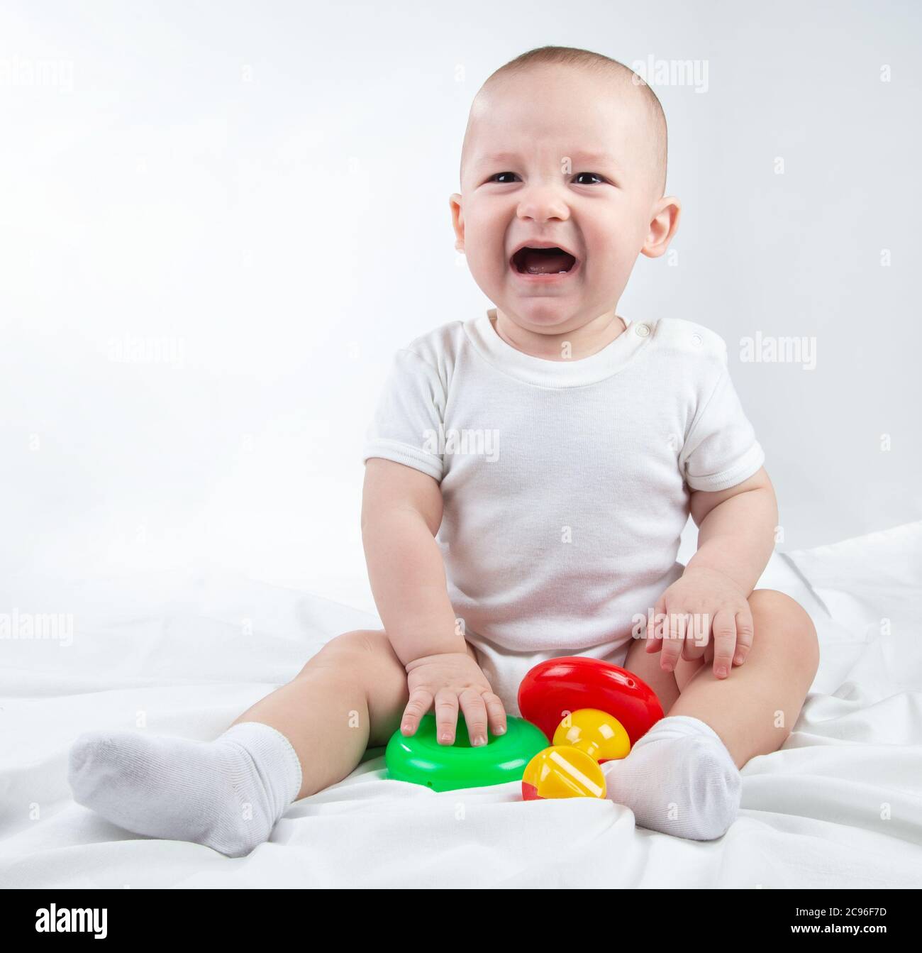 Photo of a crying nine-month-old baby with bright toys Stock Photo
