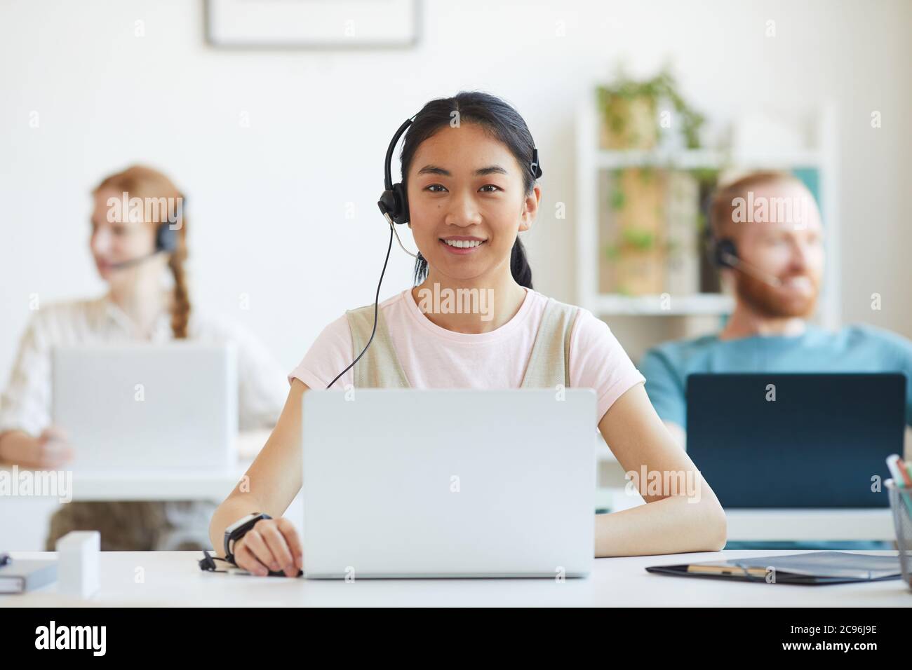 Asian young woman working in call centre, surrounded by colleagues Stock Photo