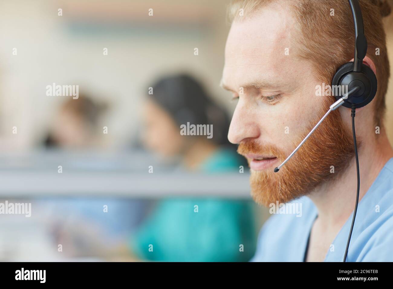 Close-up of bearded male operator using headset to talk to clients during his work in call center Stock Photo