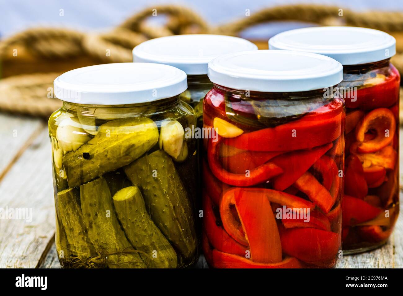 Glass jars with pickled red bell peppers and pickled cucumbers (pickles) isolated. Jars with variety of pickled vegetables. Preserved food concept in Stock Photo