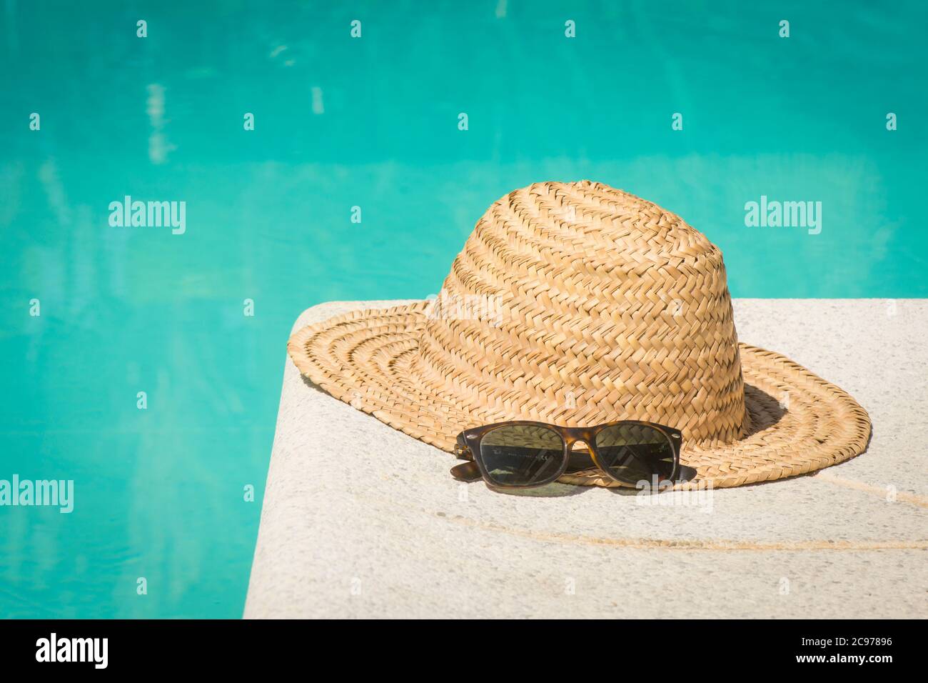 Vintage straw hat with sun glasses at the border of a swimming pool in summer. Stock Photo