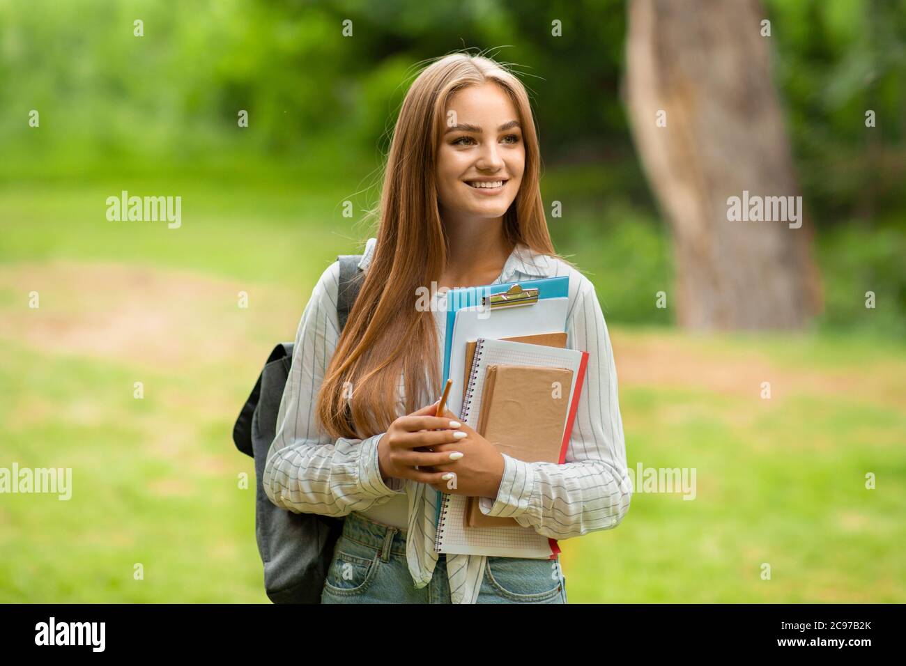 Outdoor Portrait Of Beautiful Student Girl With Workbooks And Backpack At Campus Stock Photo