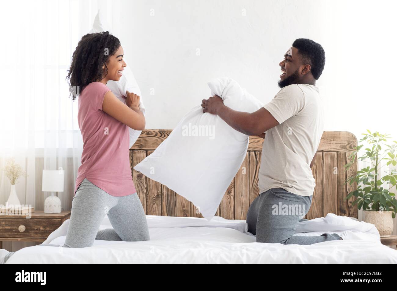 Cheerful loving black couple fighting with pillows in bed Stock Photo