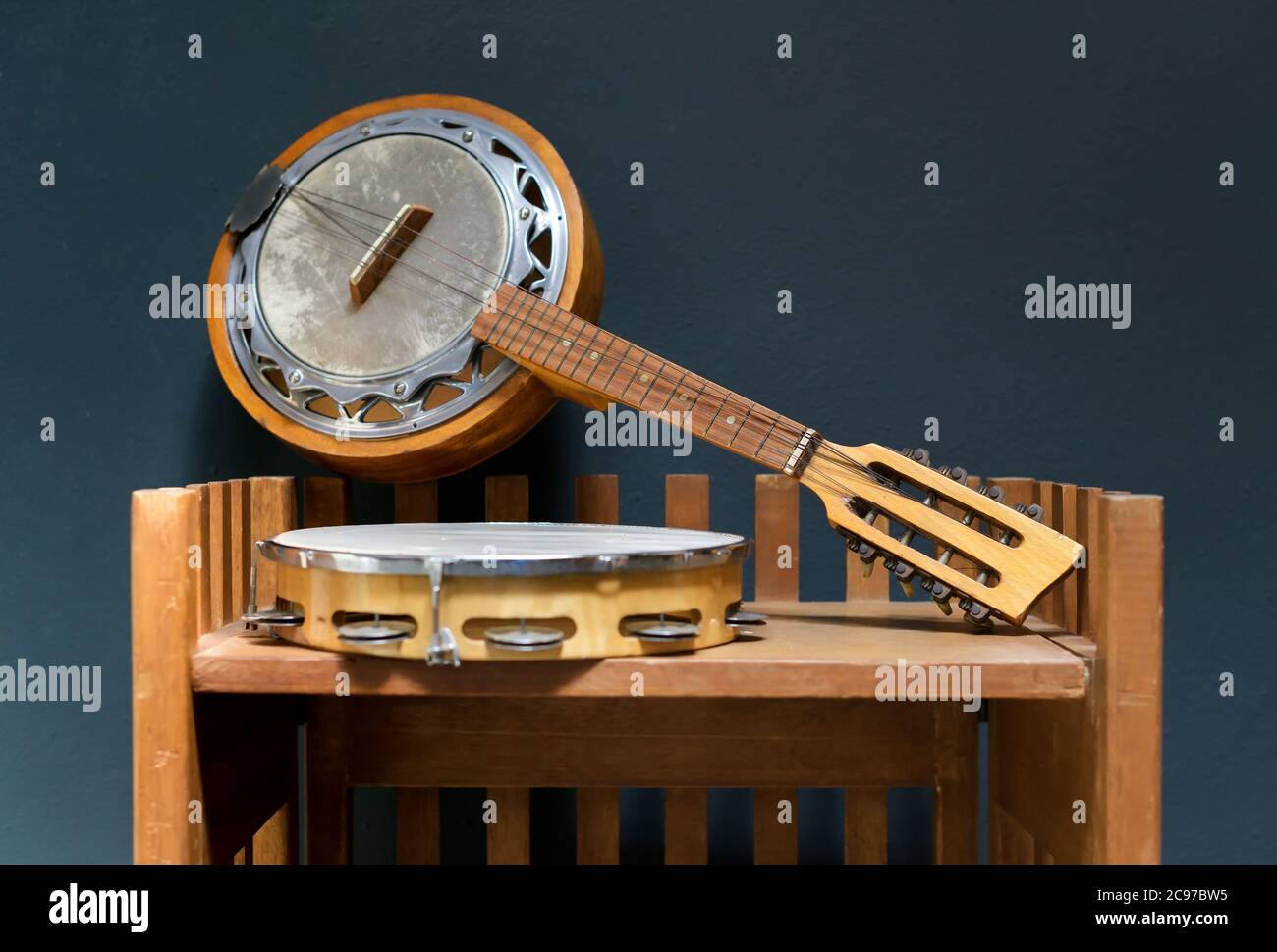 Old wooden banjo and tambourine displayed on a small shelf in close up against a grey wall Stock Photo