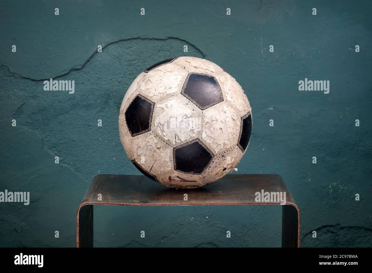 Old stained football or soccer ball on a small shelf against an old rustic green wall with missing plaster and copyspace Stock Photo