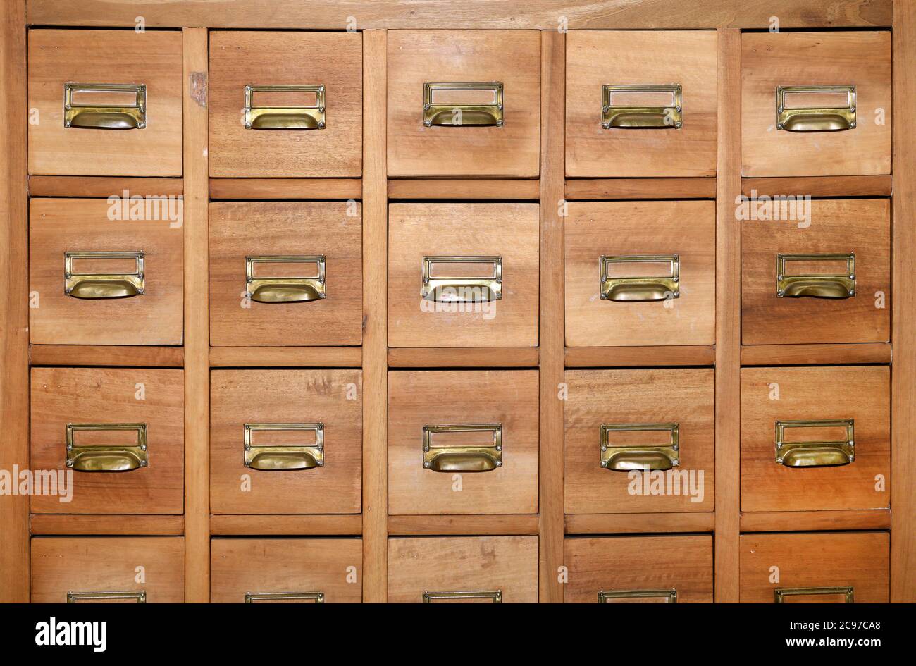 Cabinet with rows of small wooden drawers with brass handles and label holders in a symmetrical full frame background view Stock Photo