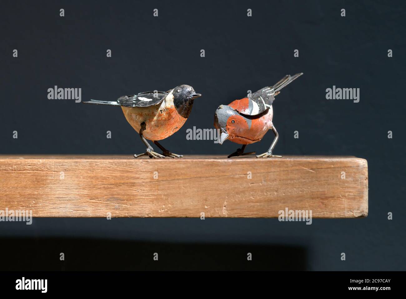 Two vintage metal toy birds on a wooden shelf, one perched and one pecking at the ground in a close up side view against black Stock Photo