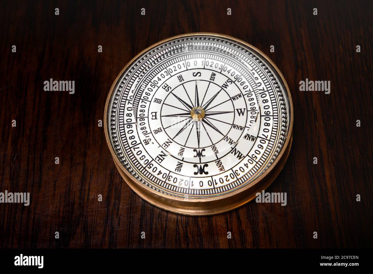 Old round brass magnetic vintage compass with glass dial lying on a wooden board in a high angle view Stock Photo
