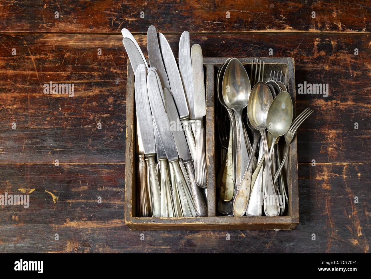 Collection of old vintage cutlery in a wooden tray with assorted silver spoons, knives and forks in an overhead view on an old rustic wooden board Stock Photo