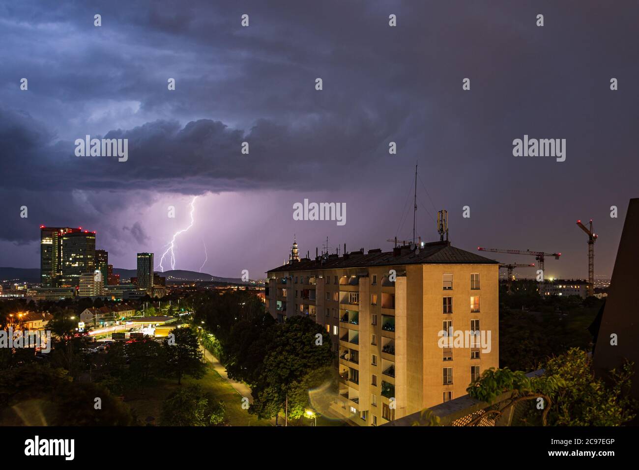 Violent summer thunderstorm with enormous lightning over the Wienerberg City in Vienna with construction cranes on the right side of the picture Stock Photo