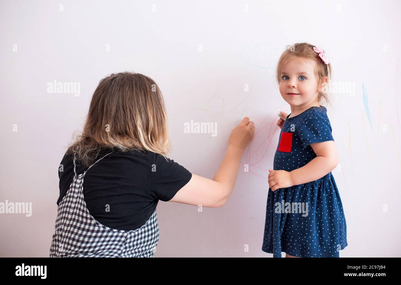 Side view of woman scolding little girl for painting walls in modern apartment Stock Photo