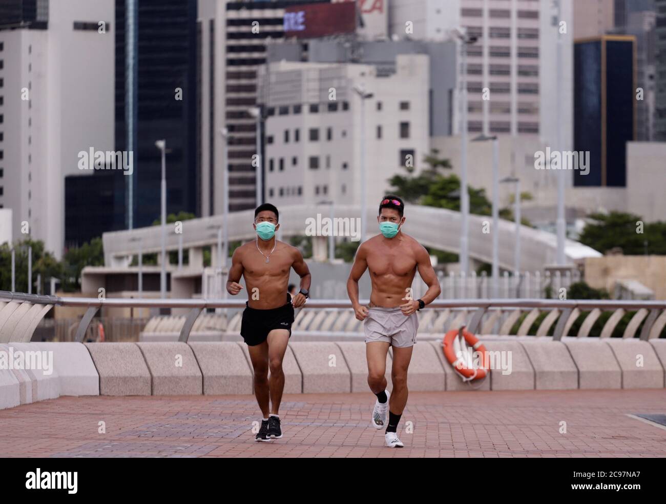 July 29, 2020, Hong Kong, CHINA: Young men jogging along Victoria Harbour waterfront promenade in Central with surgical masks on.In light of new wave of Coronavirus outbreak in the City, all citizens are ordered to wear protective masks outdoors. Those who are engaging in sports activities are not exempted under the new regulation.July-29,2020 Hong Kong.ZUMA/Liau Chung-ren (Credit Image: © Liau Chung-ren/ZUMA Wire) Stock Photo